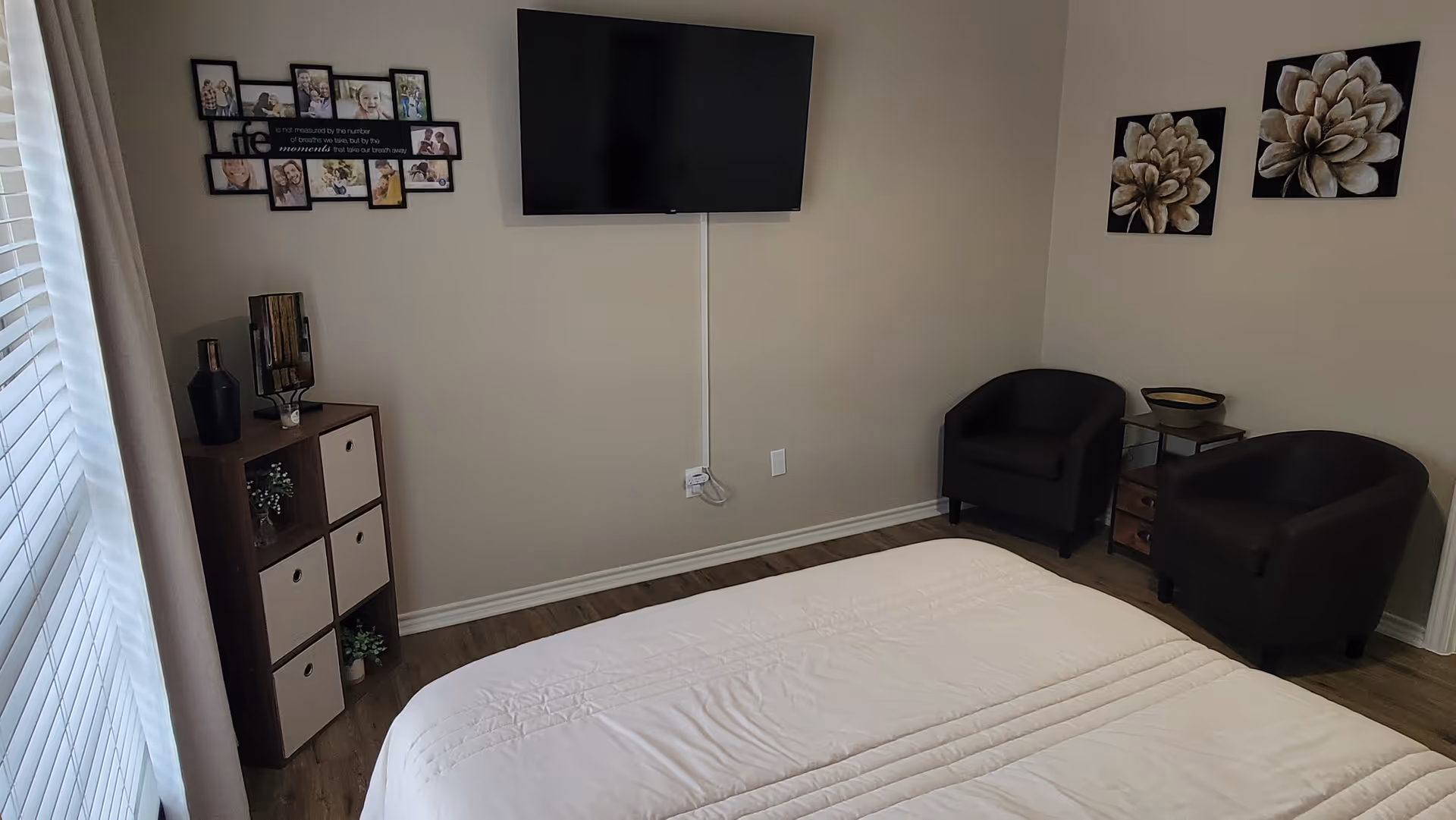 A neatly arranged senior living bedroom with bed, seating, TV, and wall decor.
