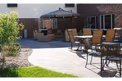 Outdoor patio with tables, chairs, and an umbrella beside a brick building.