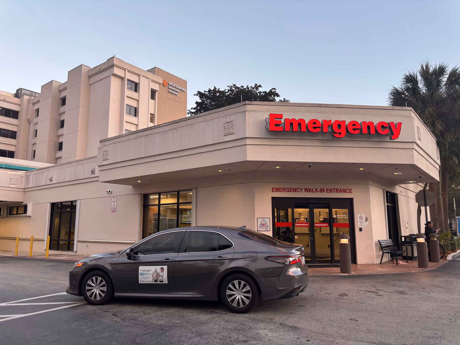 Exterior view of a medical facility with an Emergency entrance and a dark car parked outside.