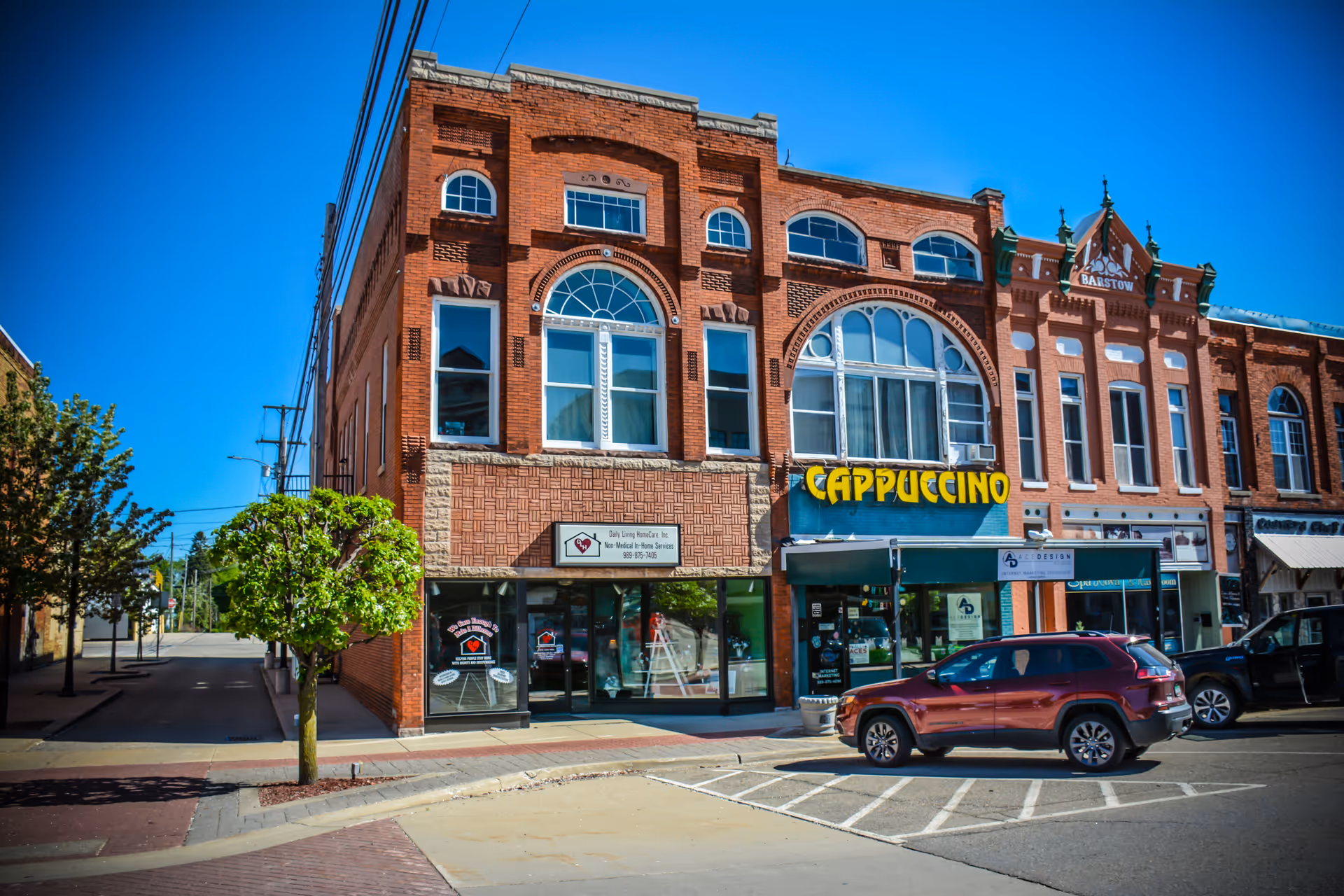 Brick building facade with storefronts and a Cappuccino sign on a sunny street.