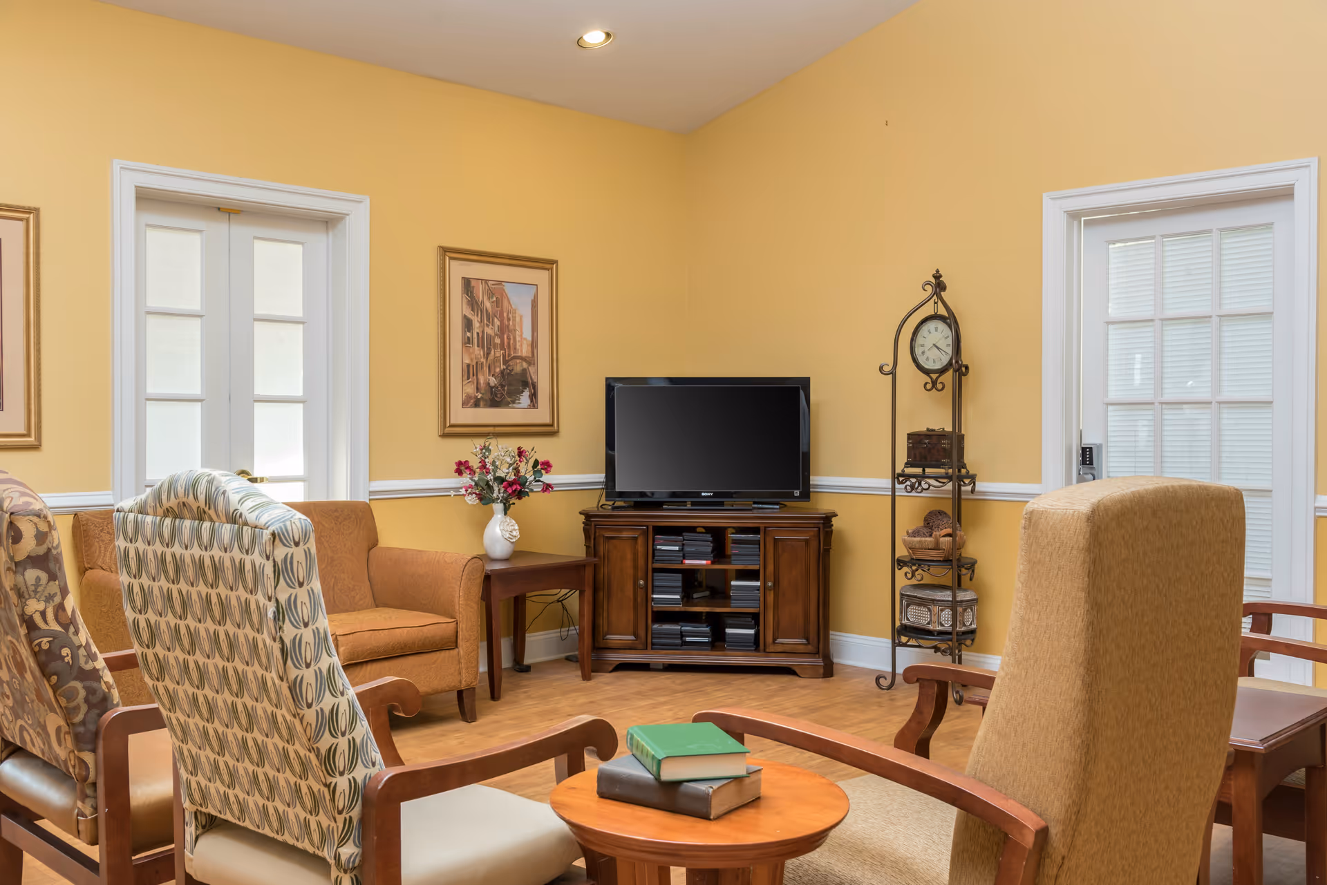 Yellow-walled living room with chairs, sofa, TV stand, and clock