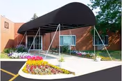 Brick exterior of a senior facility with a black curved canopy over the entrance and flowers.