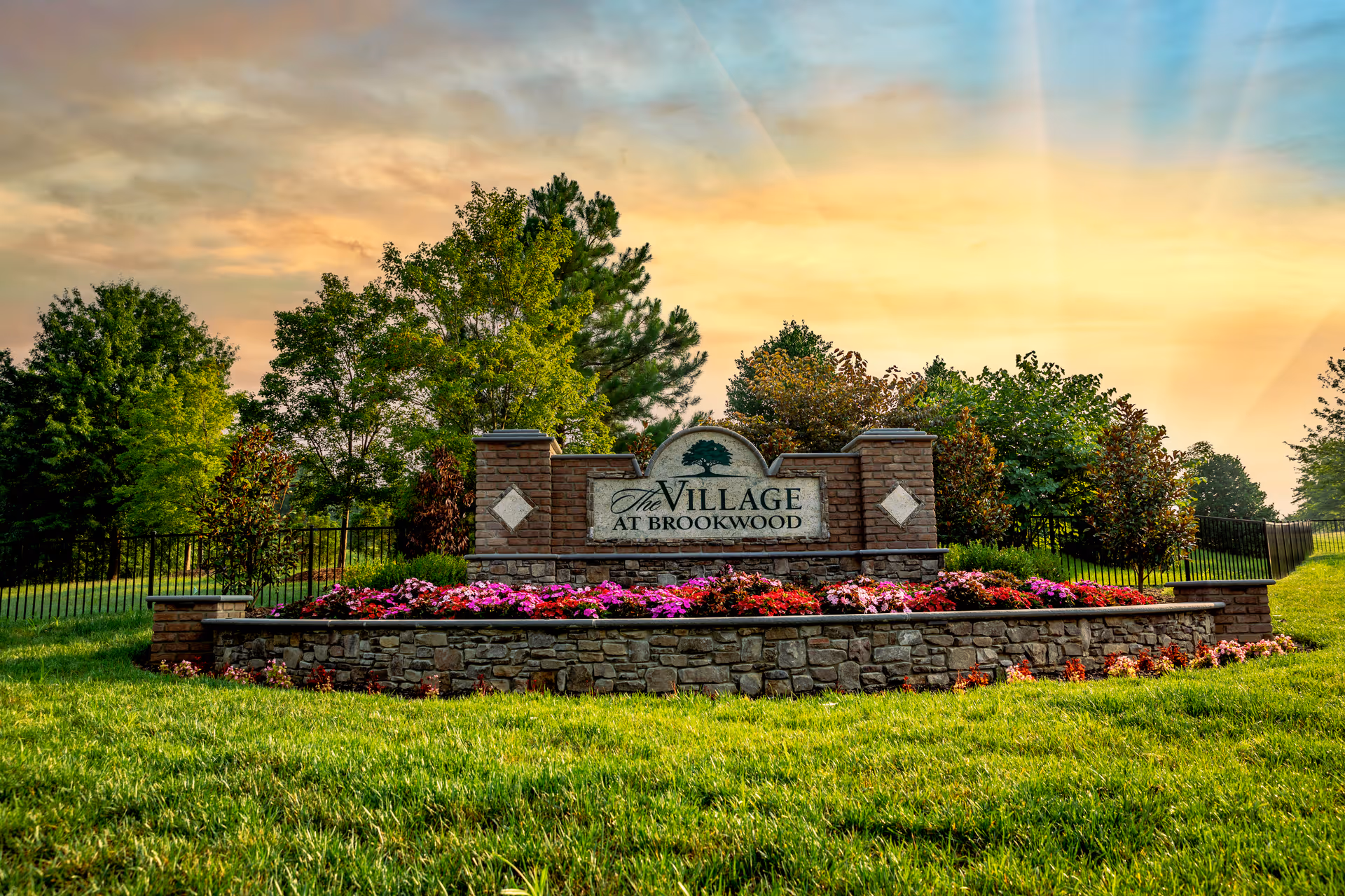 Stone sign reads The Village at Brookwood with flower beds and trees surrounding.