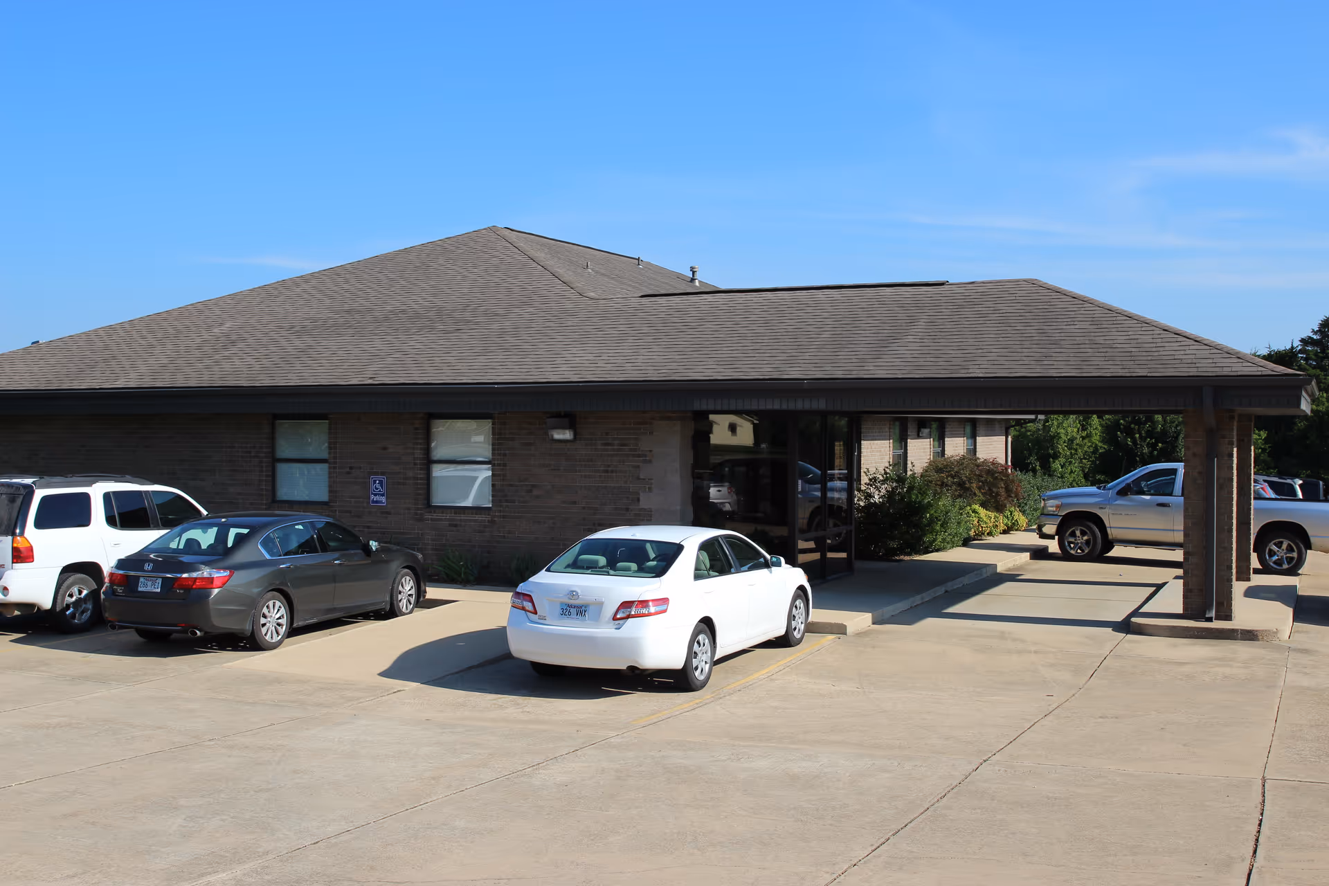 Single-story brick building with a covered entrance and several parked cars.