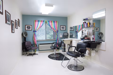 Small salon room with styling chairs, mirrors, a sink and colorful curtains at a window.