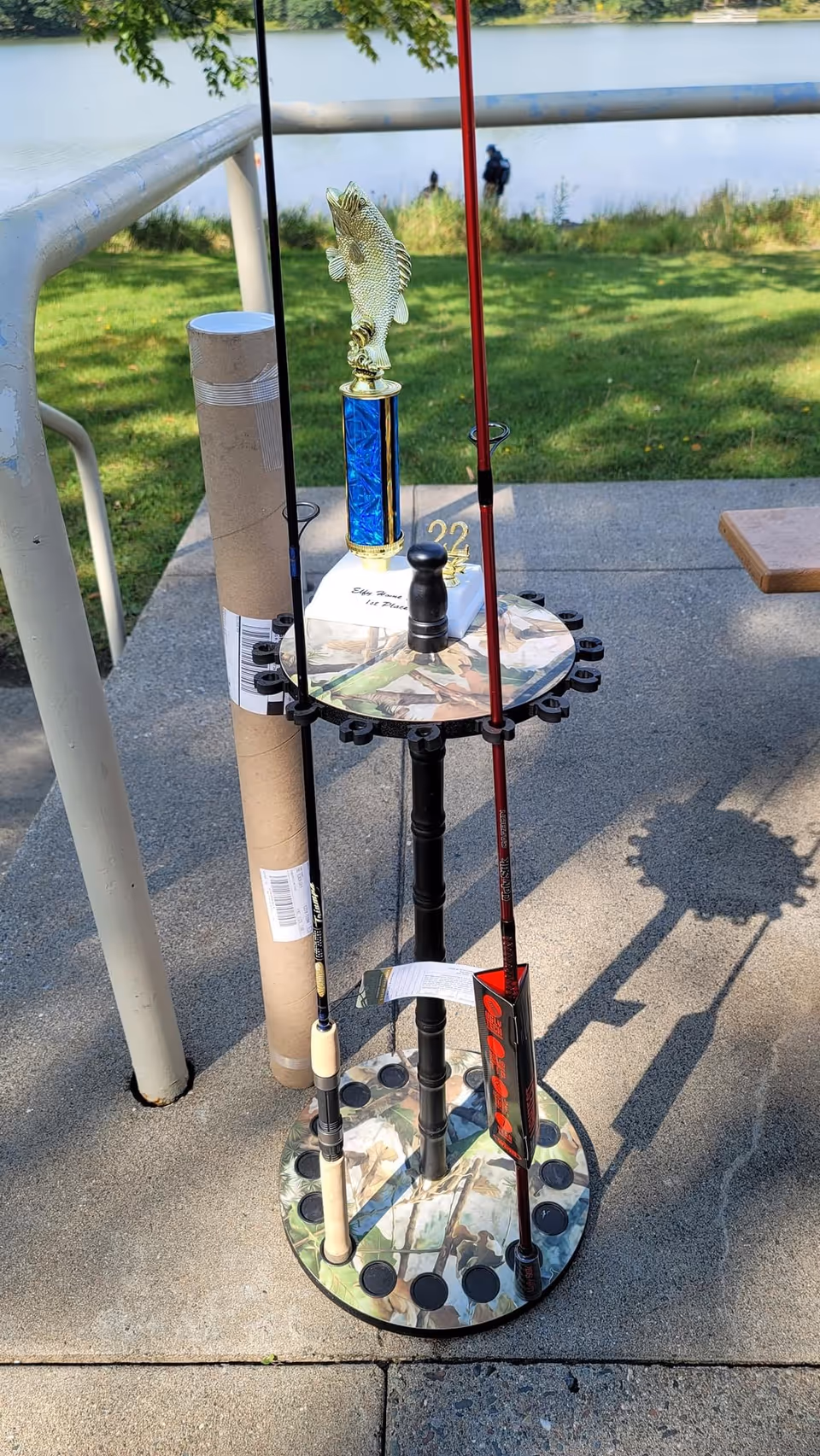 Outdoor display of fishing rods and a trophy on a stand near a railing.
