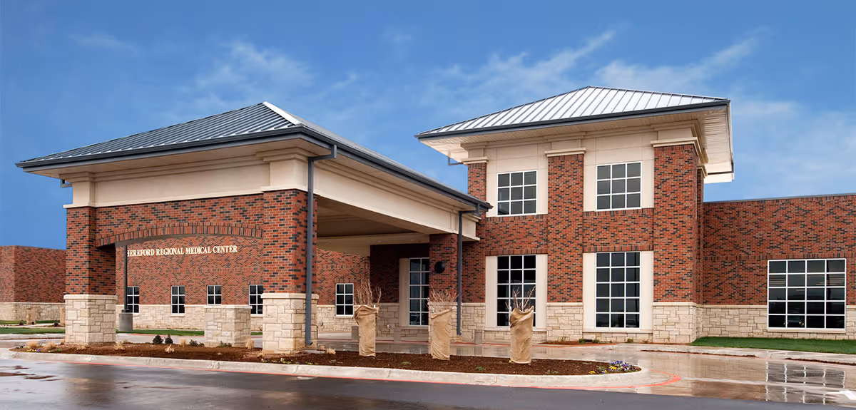 Brick hospital-style building with covered entrance and multiple windows against a blue sky.