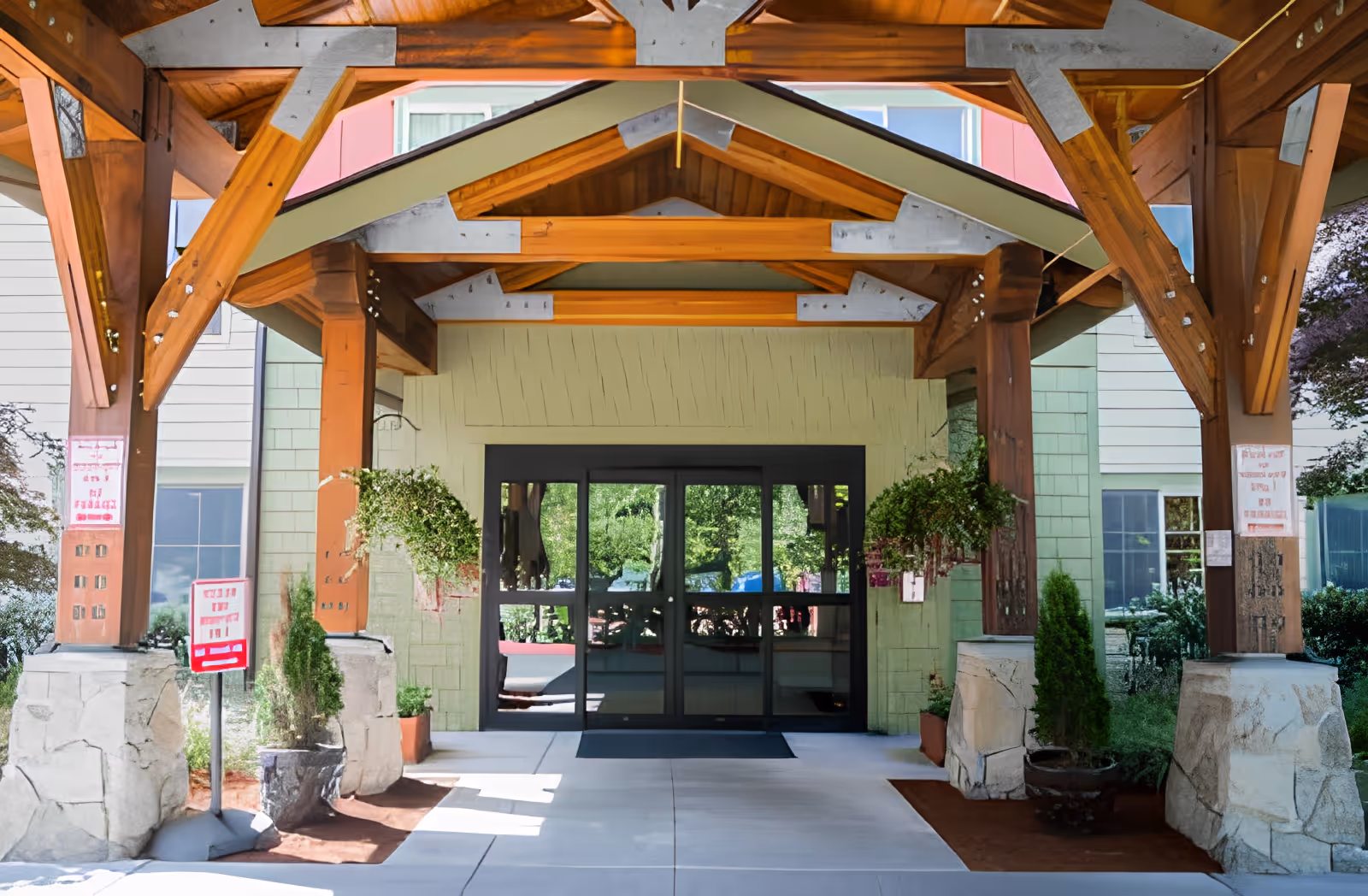 Covered timber portico with hanging plants leading to glass entrance doors of a building.