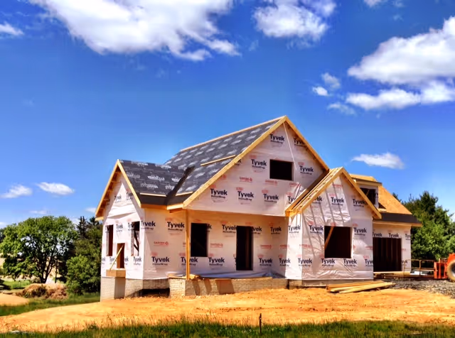 Under-construction residential building wrapped in Tyvek under a blue sky