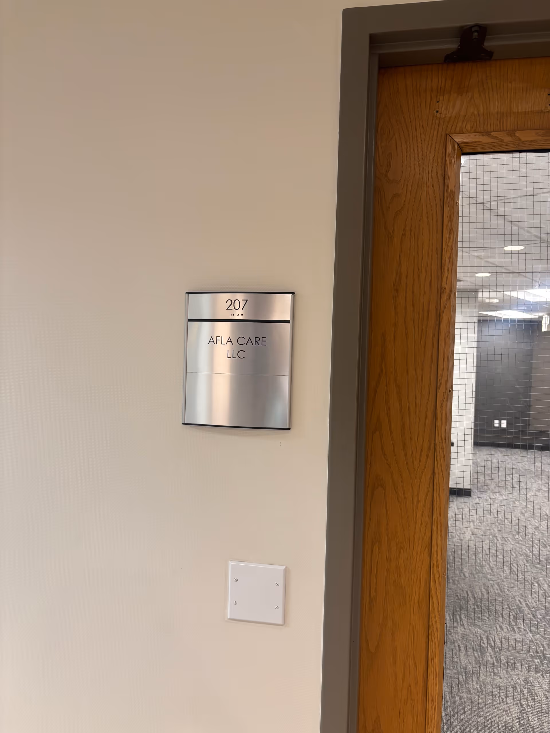 Metal plaque on wall reads AFLA CARE LLC with room 207 beside a wooden door