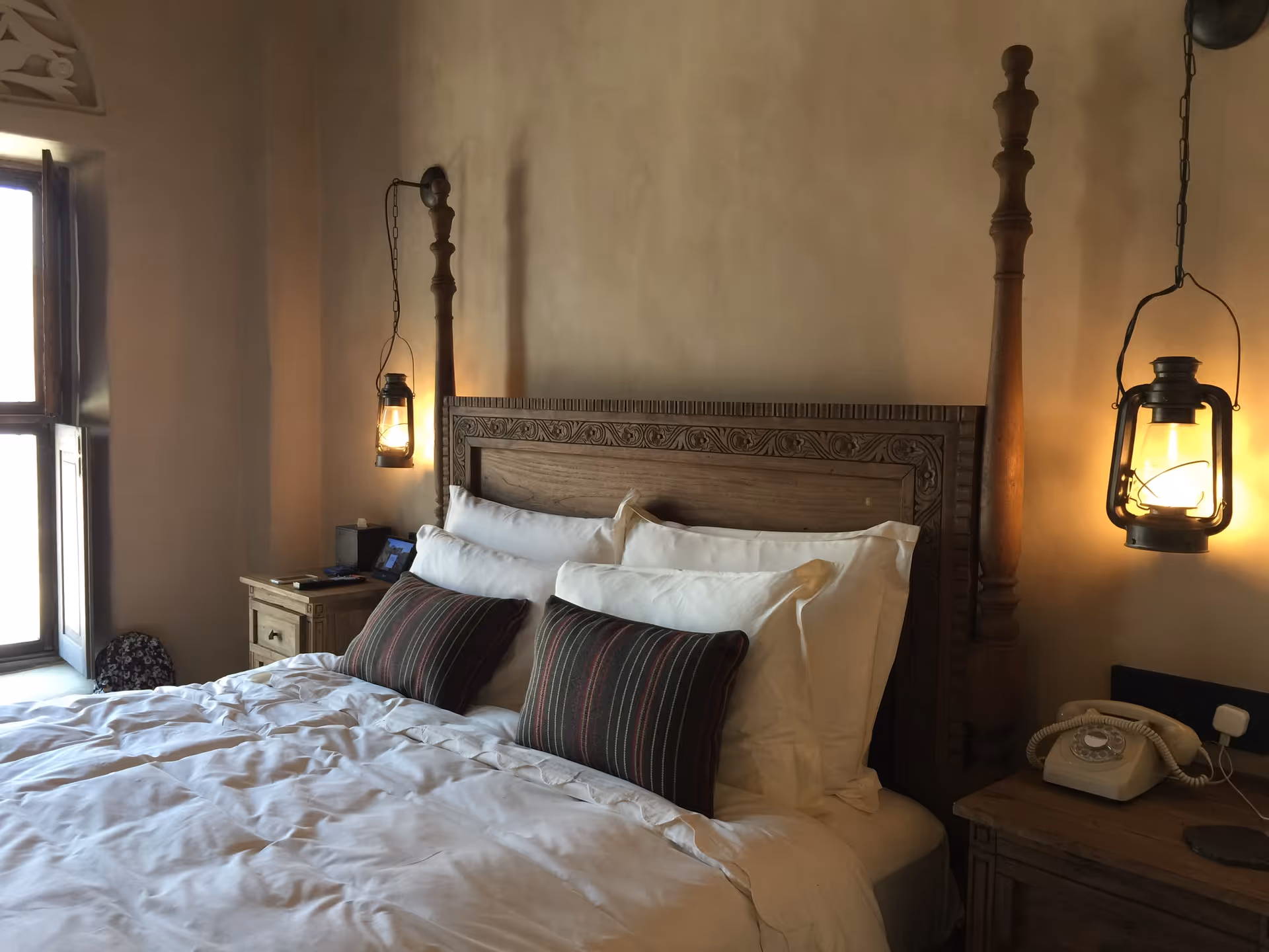 A four-poster bed with carved headboard, nightstands, and warm hanging lanterns.