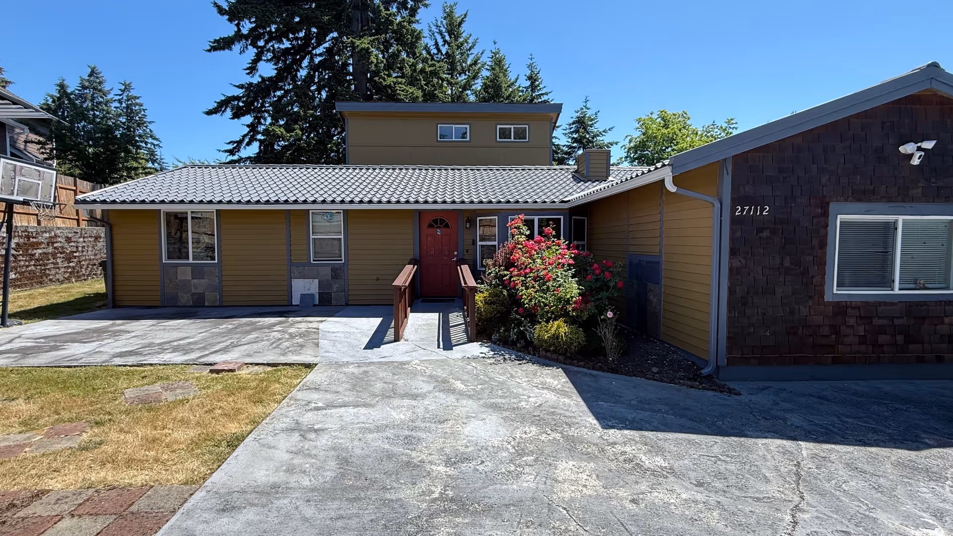 Exterior view of a single-story facility with a red front door and flowering shrubs.