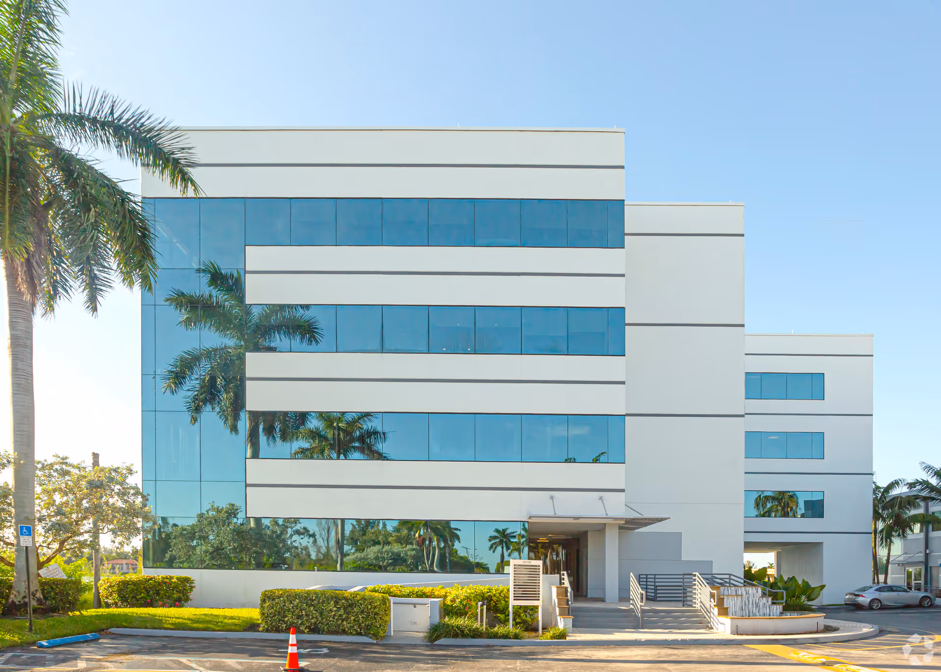 Modern glass-front facility facade with palm trees and a sunlit entrance.