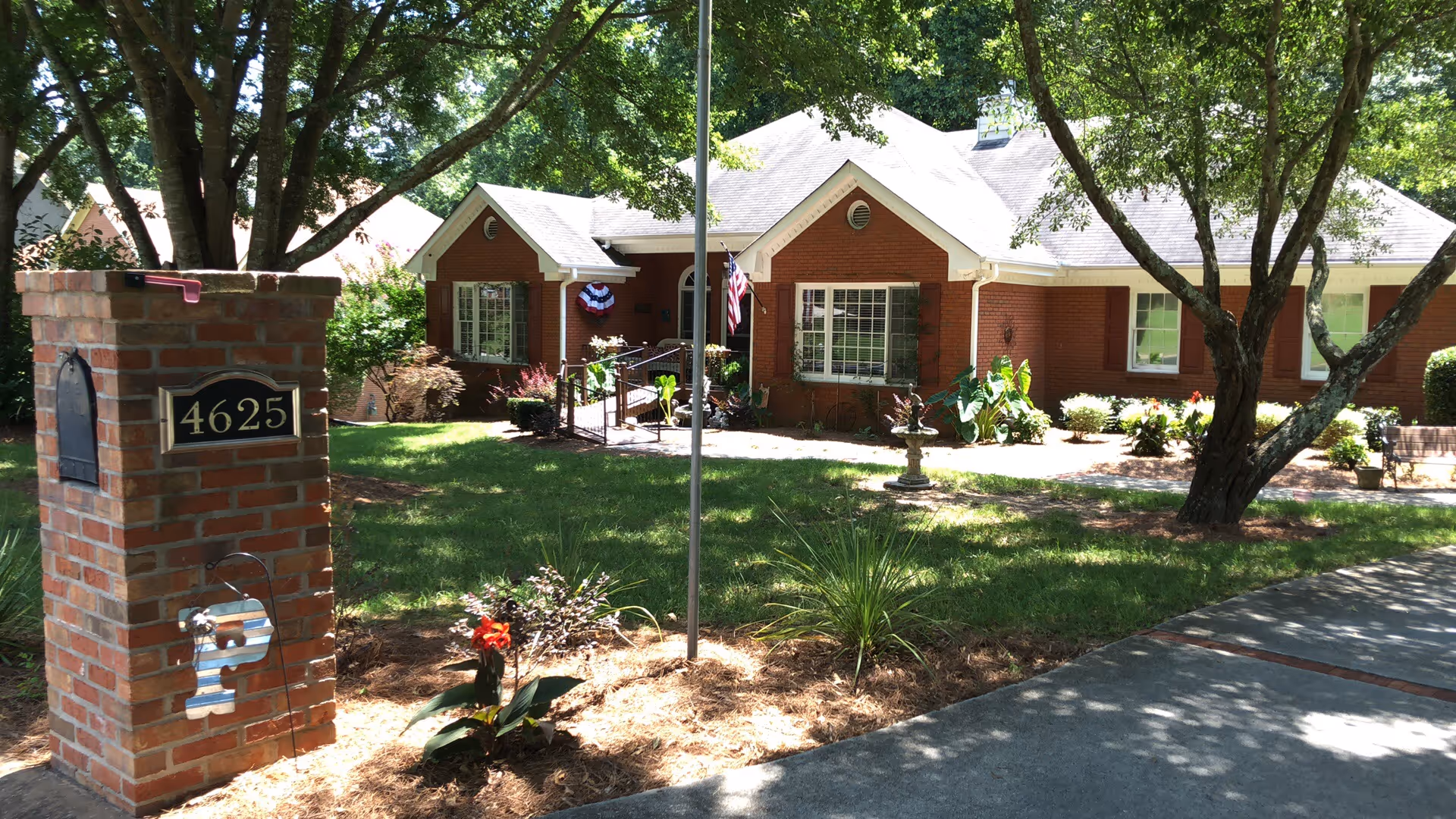 Brick senior care facility with manicured lawn, front entrance, and surrounding trees.