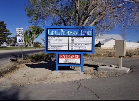 Outdoor view of a blue Calvada Professional Center sign near a road.