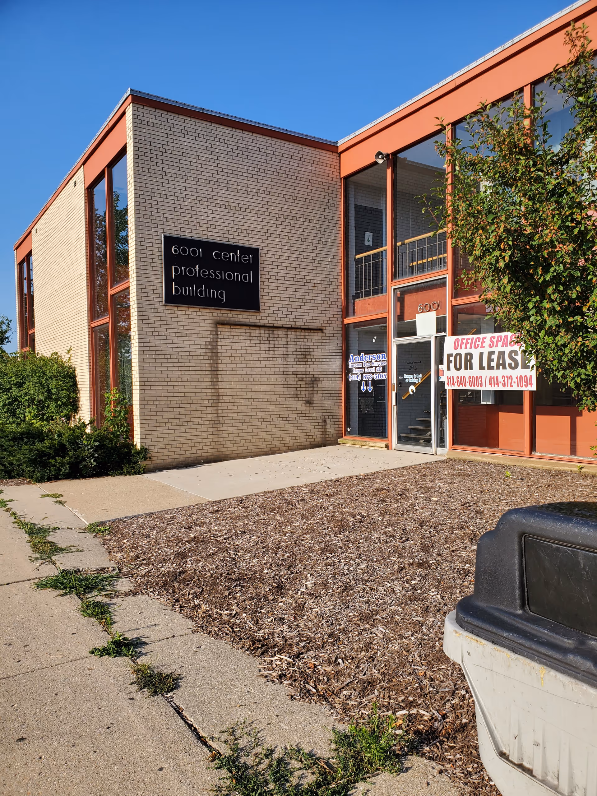 Exterior view of a brick building with glass storefront and a lease sign.