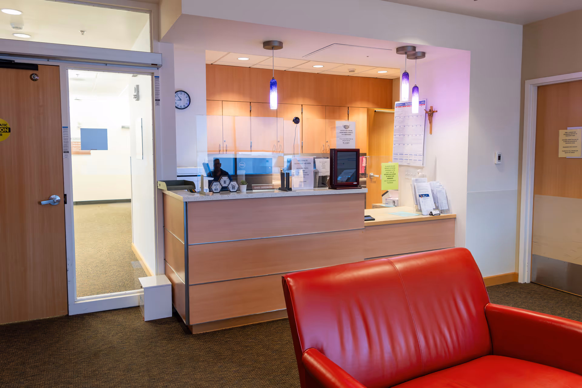 Reception desk with wood panels, purple pendant lights, and a red leather sofa in lobby