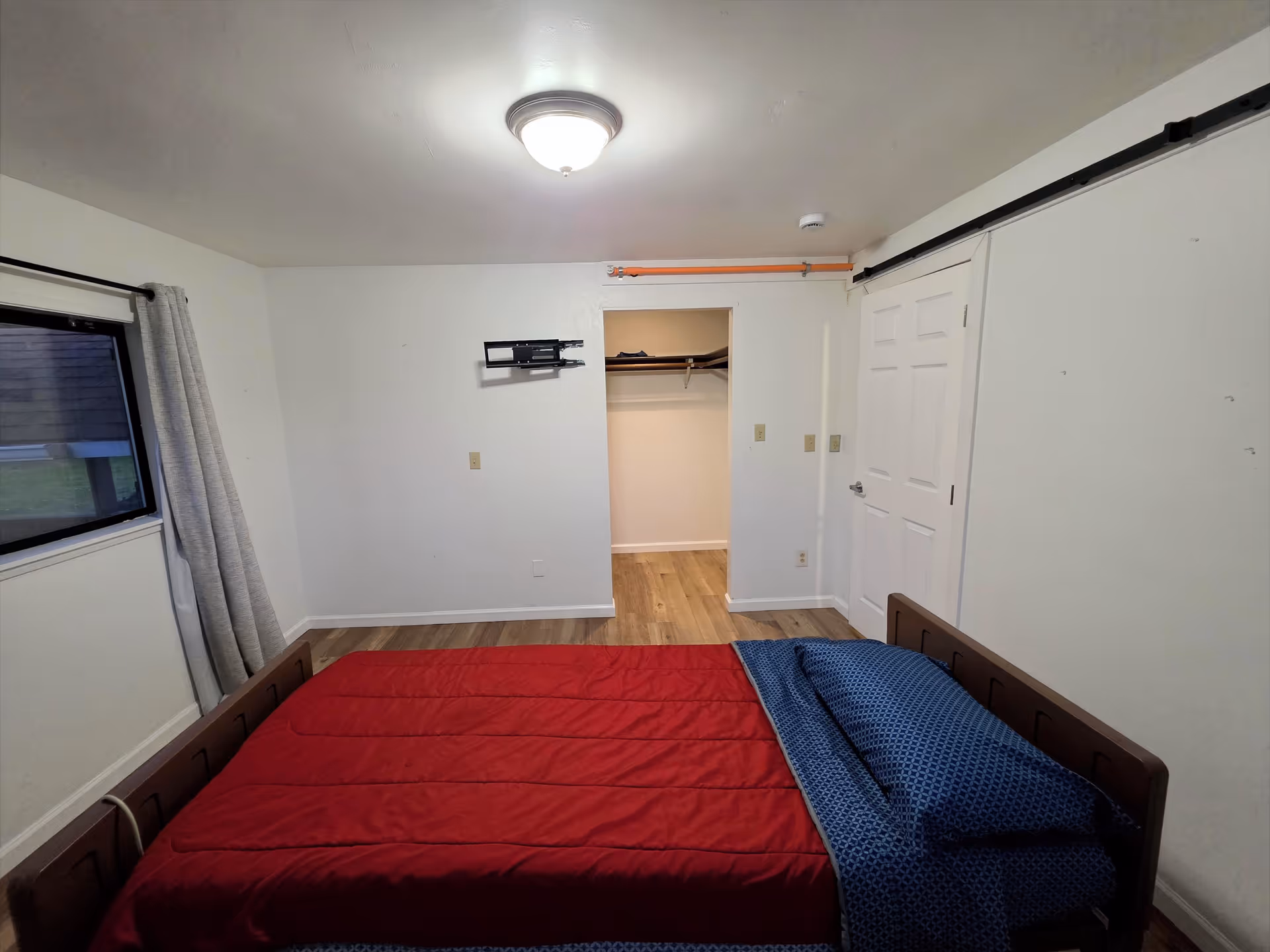A plain bedroom with a bed, window with curtains, and a closet at the far wall.