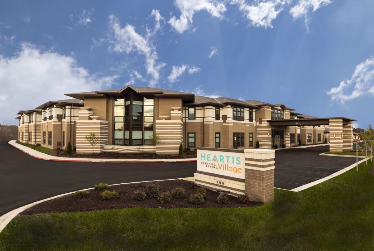 Exterior front view of a two-story senior living building with a landscaped driveway and a 'HEARTIS Village' sign.