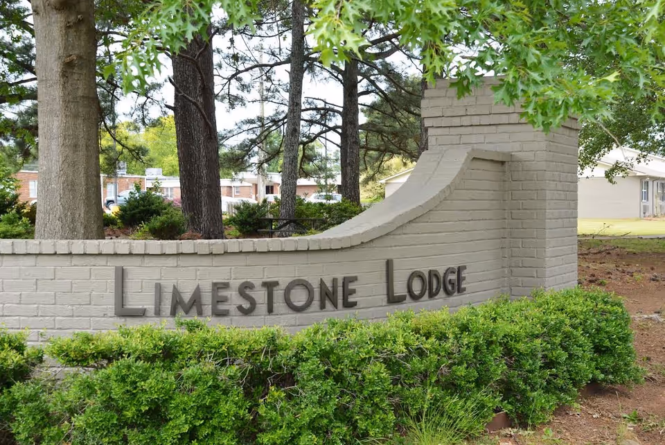 Entrance sign reading Limestone Lodge on curved brick wall with green hedges.