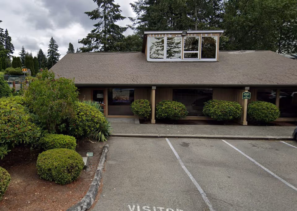 Front exterior of a single-story building with shrubs and a parking area.