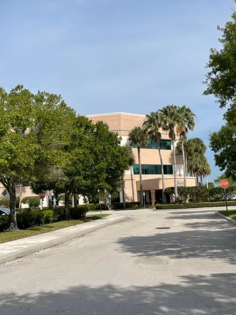 Exterior view of a senior living facility with palm trees and a driveway.
