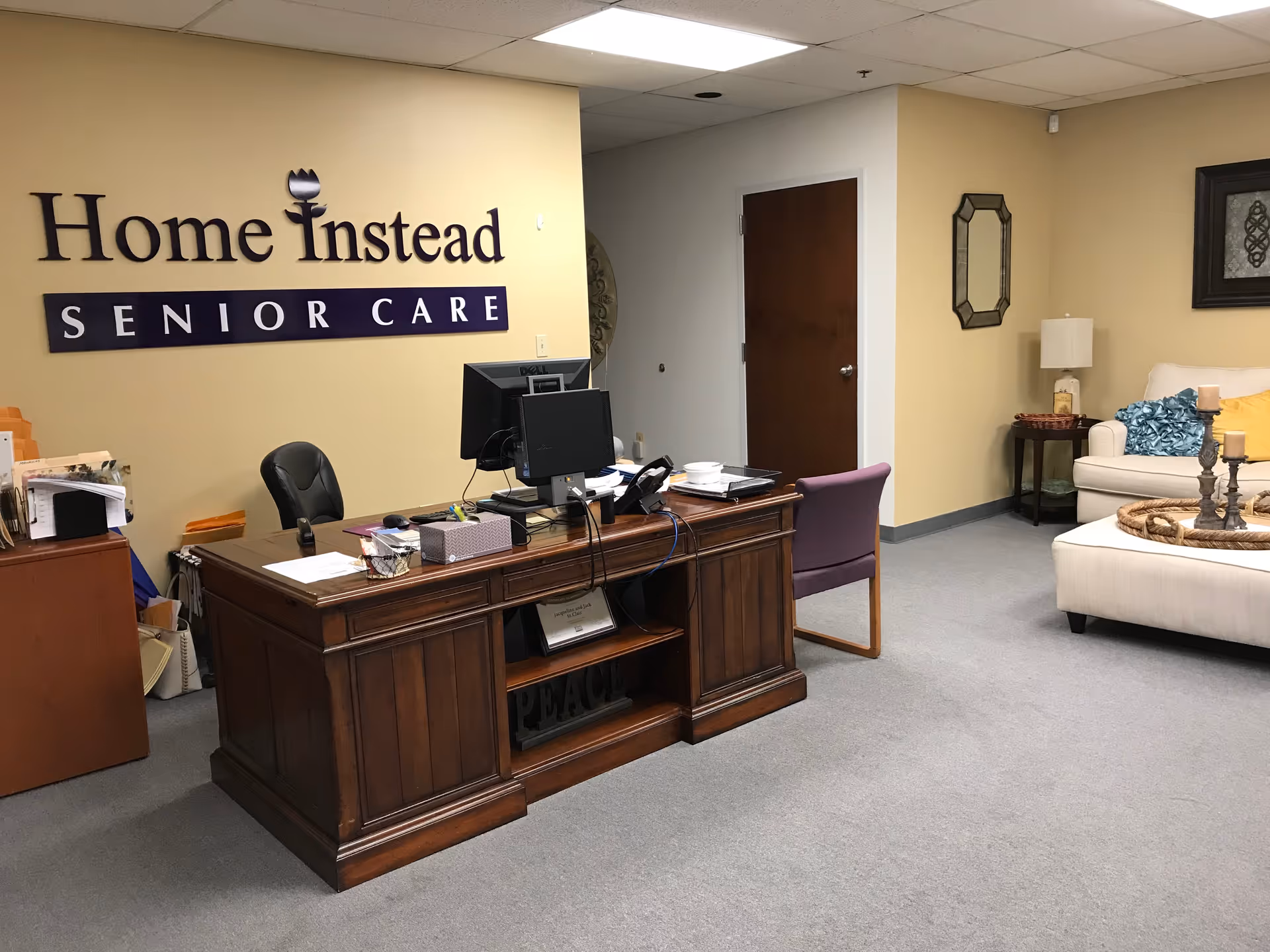 Reception area with a wooden desk and Home Instead Senior Care sign in beige lobby.