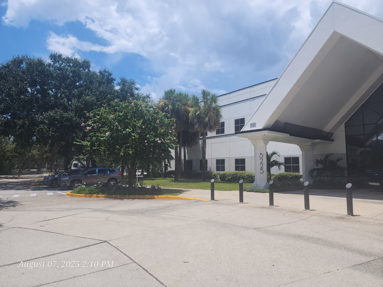 Exterior view of a modern facility entrance with trees, parking, and a covered drop-off.