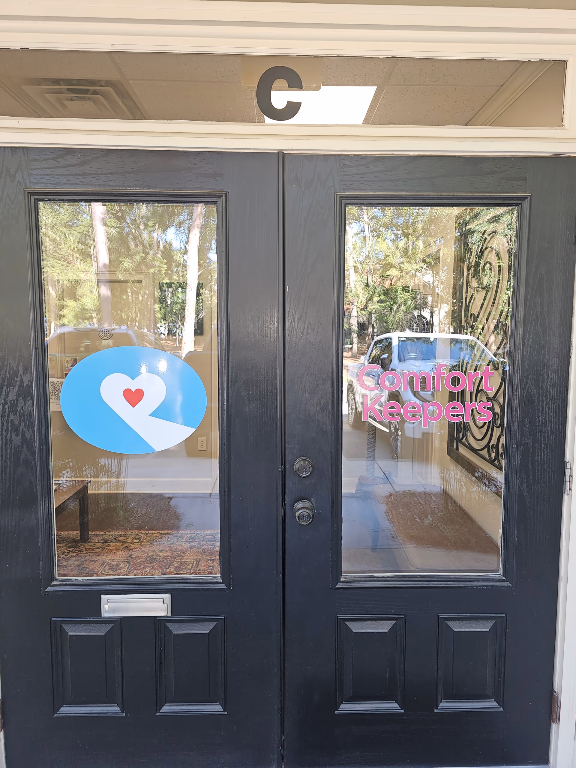 Double gray entrance doors with Comfort Keepers signage, a blue heart logo, and 'C7' above.