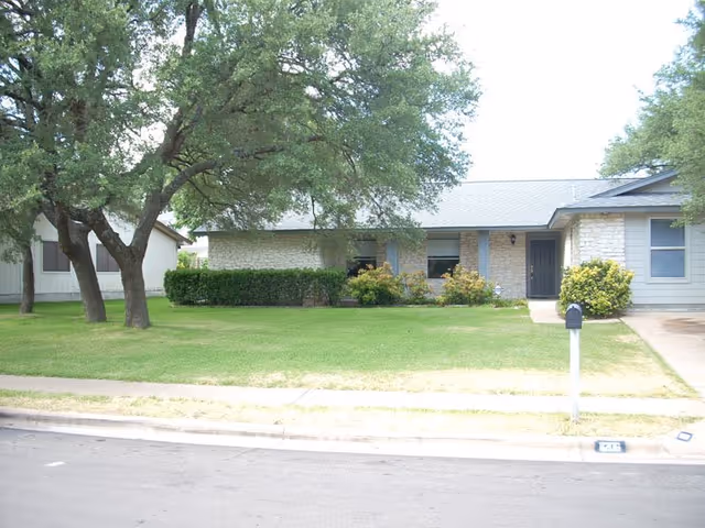 Exterior view of a single-story senior living facility with a front lawn and trees.