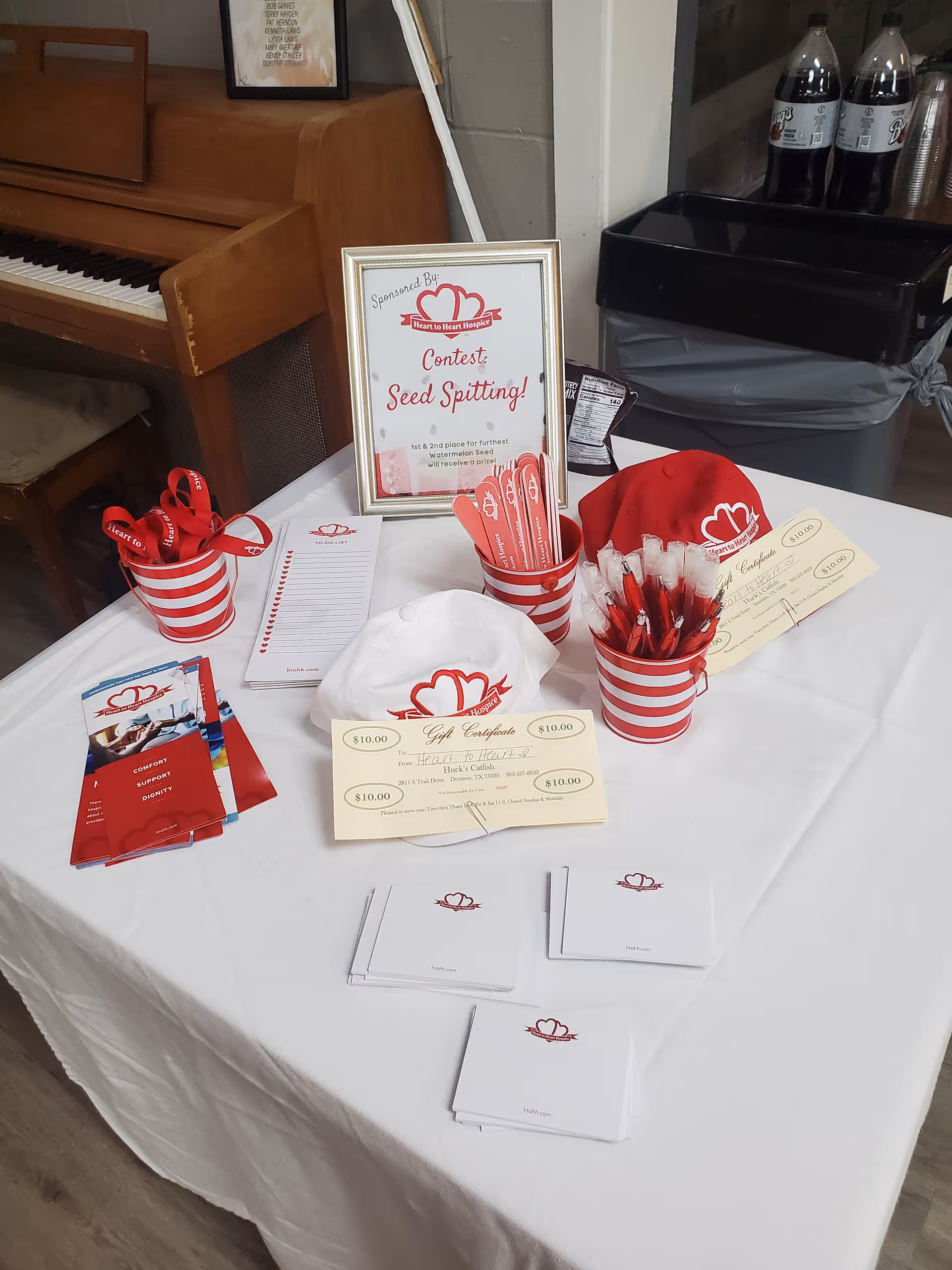 Promotional table with Heart to Heart Hospice materials, red striped cups, flyers, and a framed sign.
