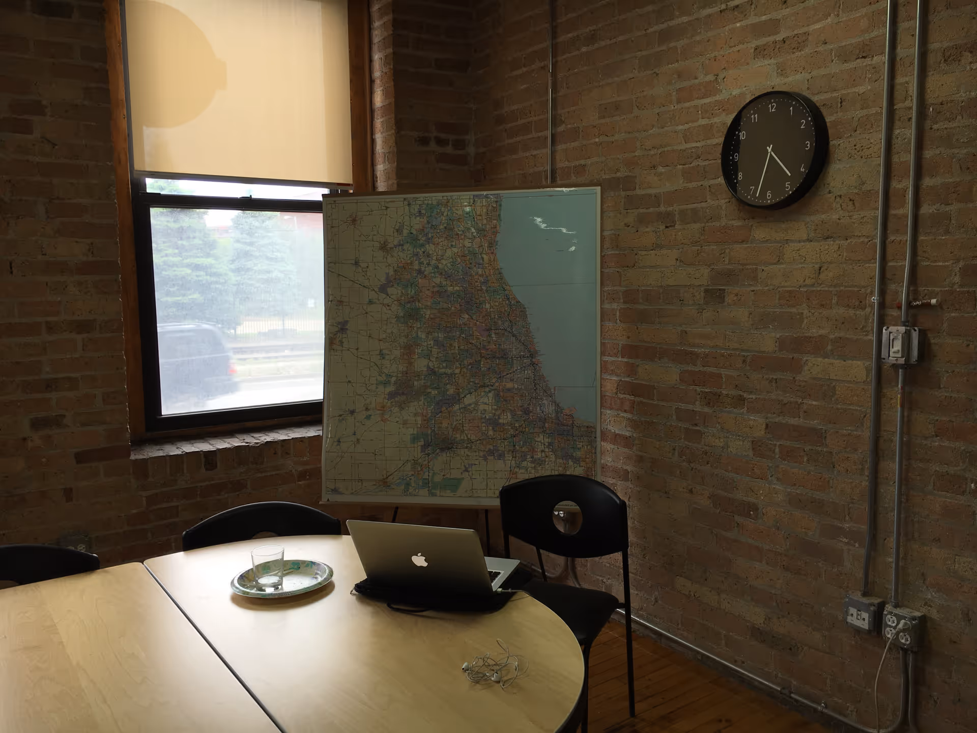 A brick-walled conference room featuring a round table, laptop, large map, and a wall clock.