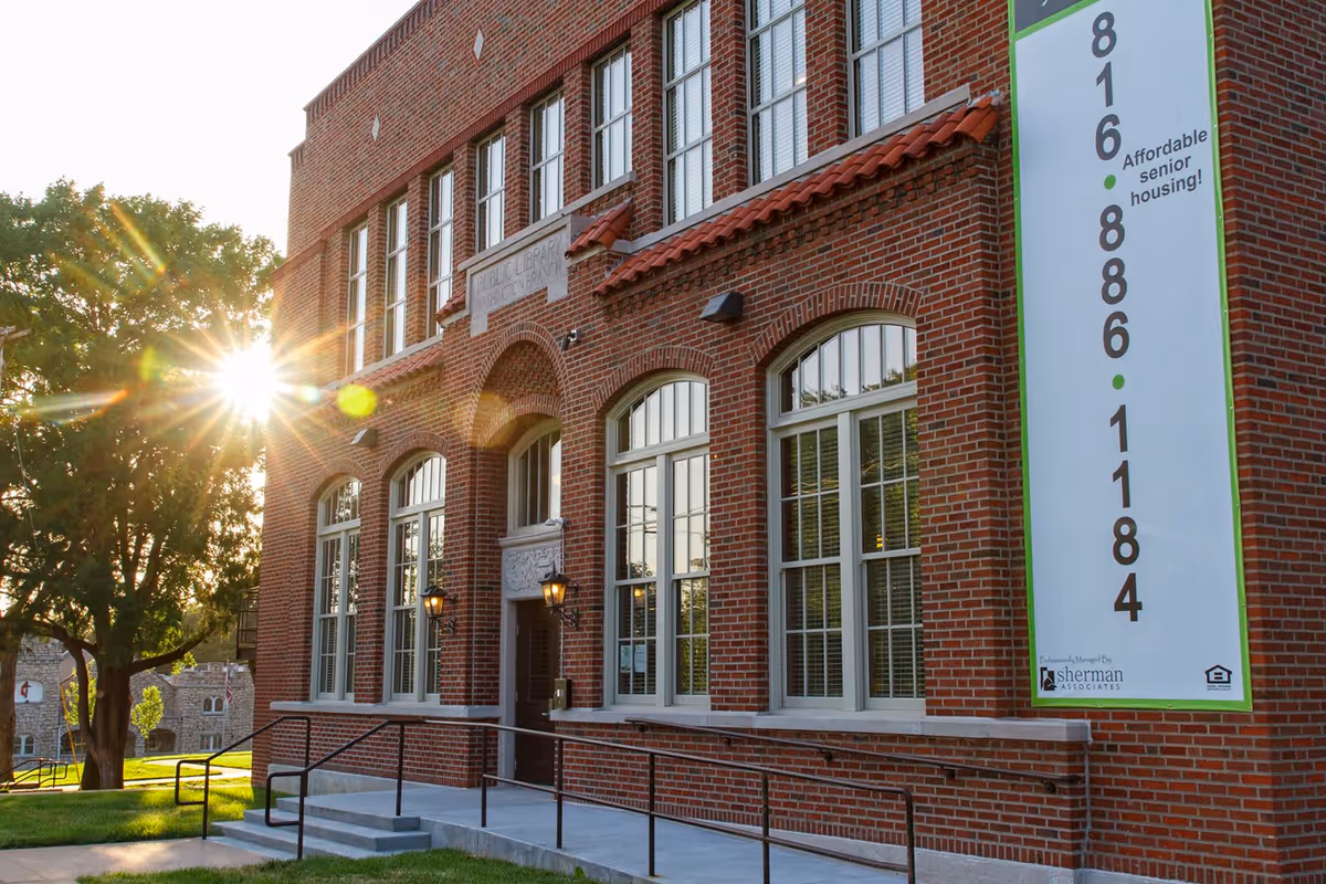 Sunlit red-brick building facade with arched windows and a tall banner advertising affordable senior housing.