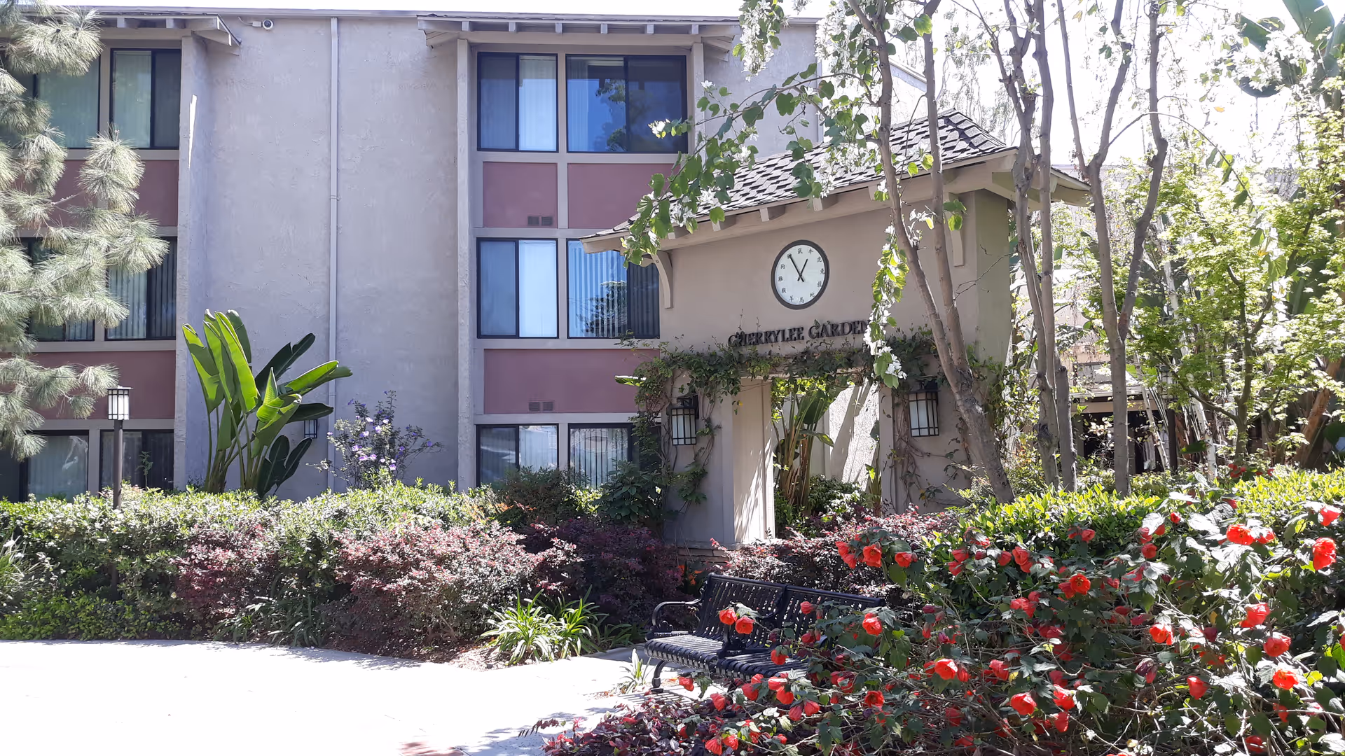 Exterior view of a senior living facility with a clock, entrance, and blooming garden.