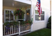 Beige building entrance with a small porch, hanging flower baskets, and an American flag