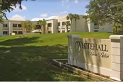 Exterior view of a beige rehabilitation building with a manicured lawn and stone sign.