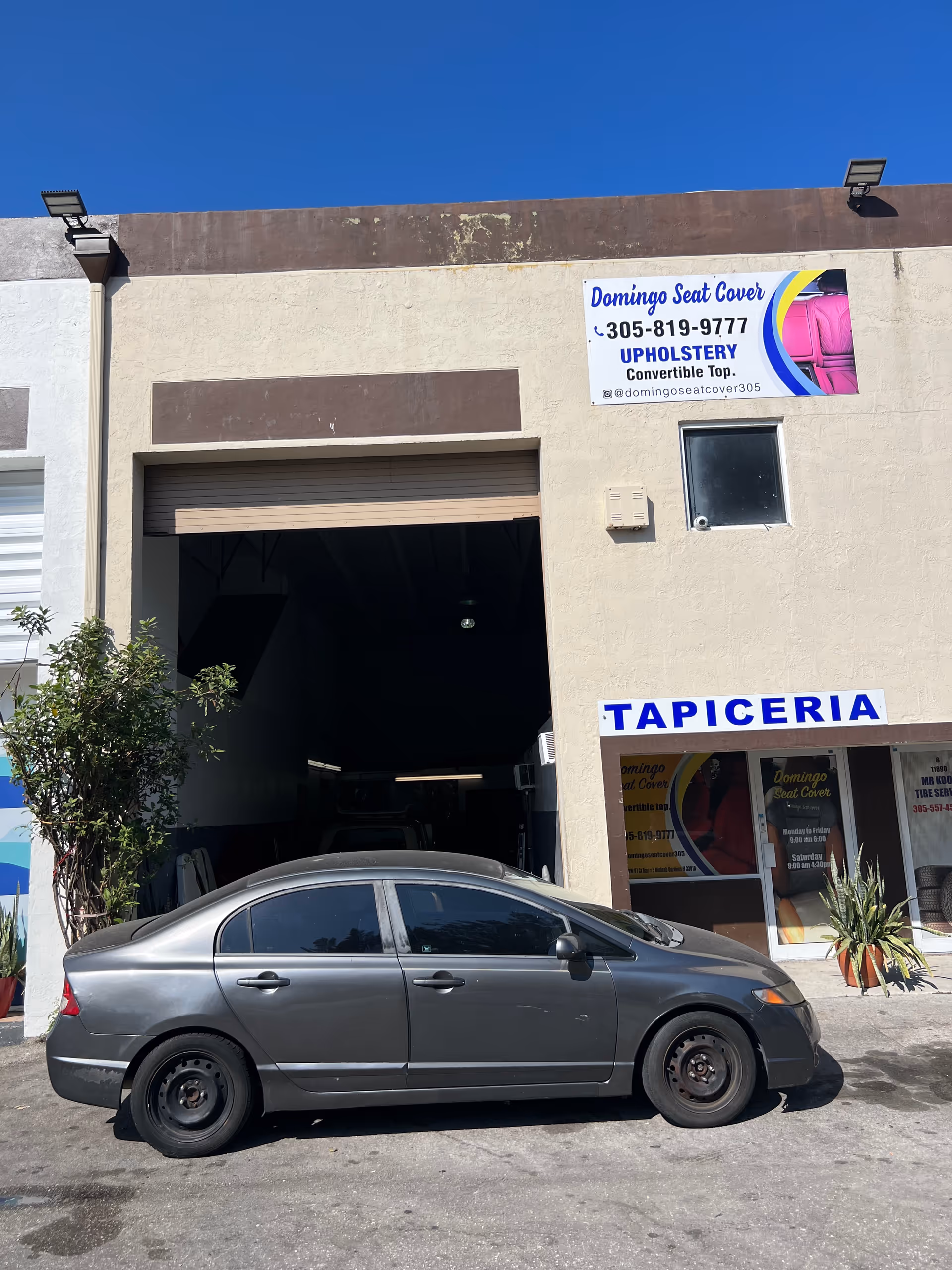 Silver sedan parked in front of a beige building with upholstery shop signage.