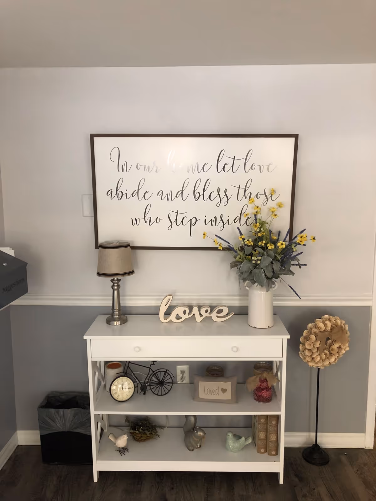 Framed wall art above a white console table with a lamp, vase of flowers, and decor