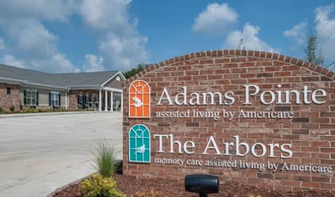 Exterior view of Adams Pointe facility with a brick sign and building in background.
