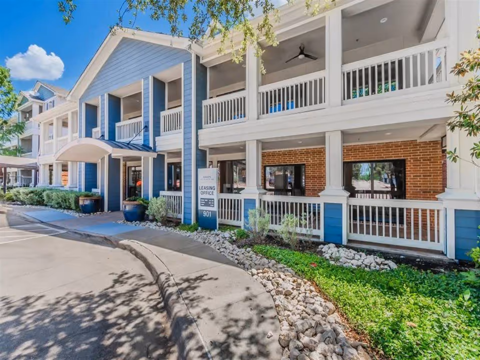 Blue and white senior living building facade with balconies and a leasing office sign.