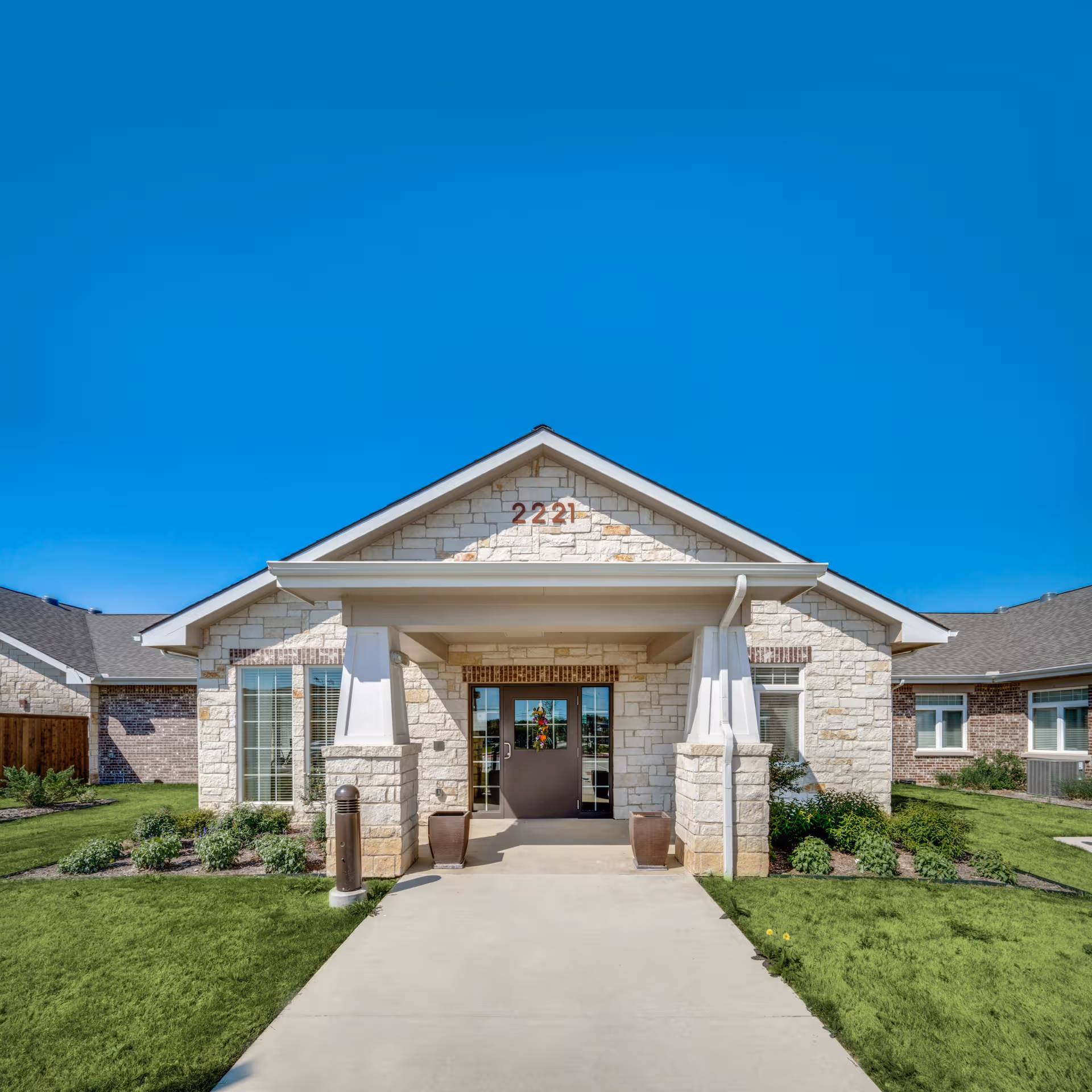 Front view of Oxford Glen Memory Care entrance, a stone building under a bright blue sky.