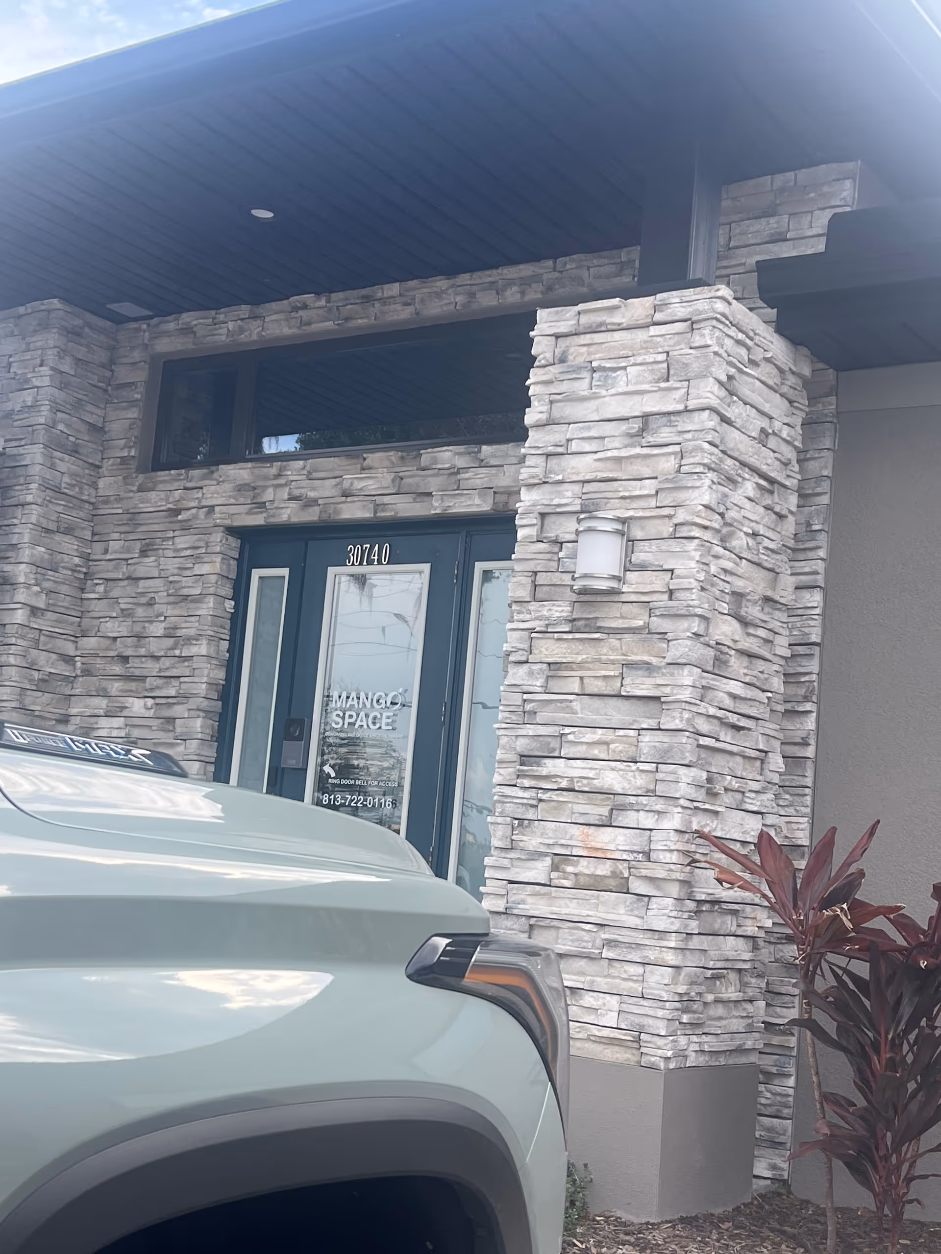 Stone-clad building entrance with glass doors and a light-colored SUV parked in front.
