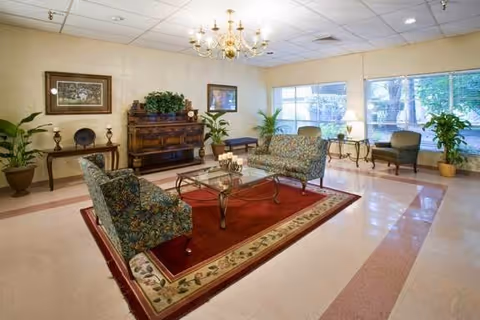Bright indoor living room lounge with seating, plants, and a chandelier.