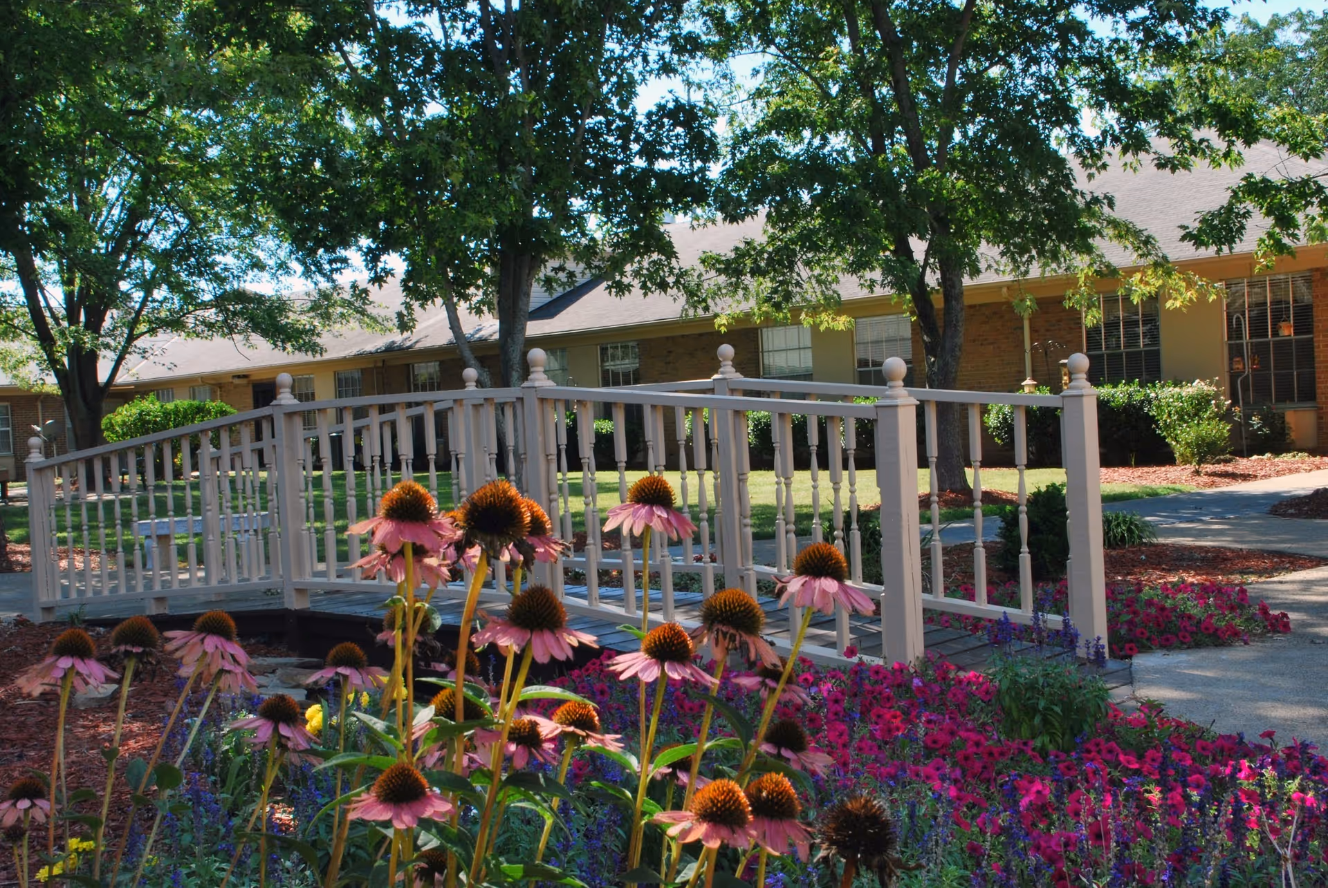 Exterior view of a senior living facility with a white railing bridge and colorful flowers.