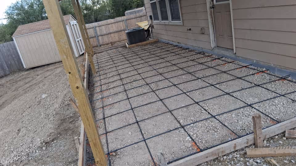 Backyard patio under construction with a metal rebar grid beside the house.