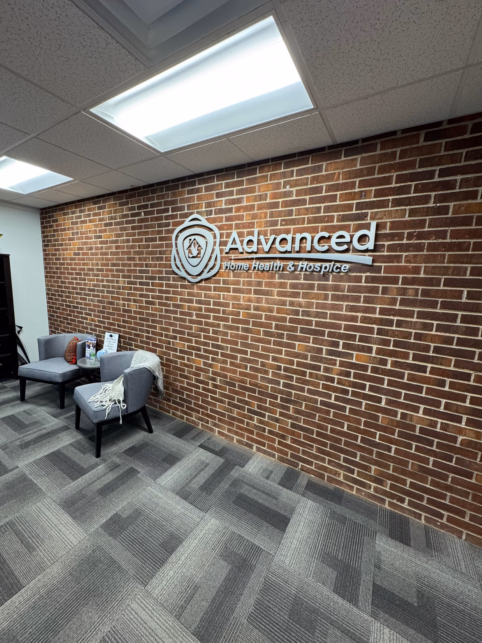 Lobby seating area with brick wall logo for Advanced Home Health & Hospice.