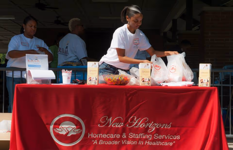 Staff organize items at an outdoor booth with a red New Horizons banner.