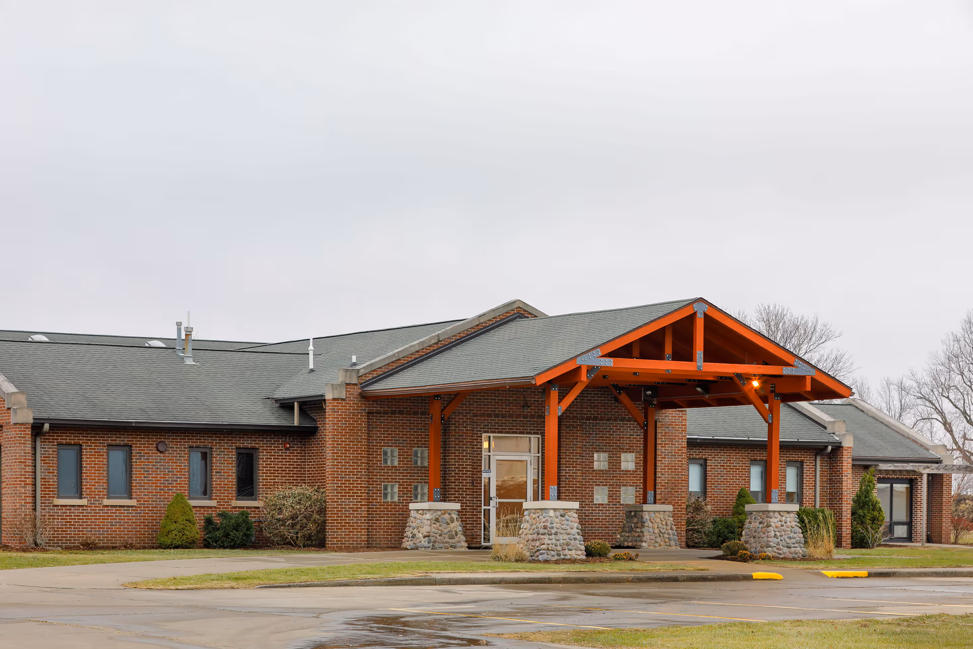 Brick senior living facility with a covered entry, stone pillars, and a paved parking area.