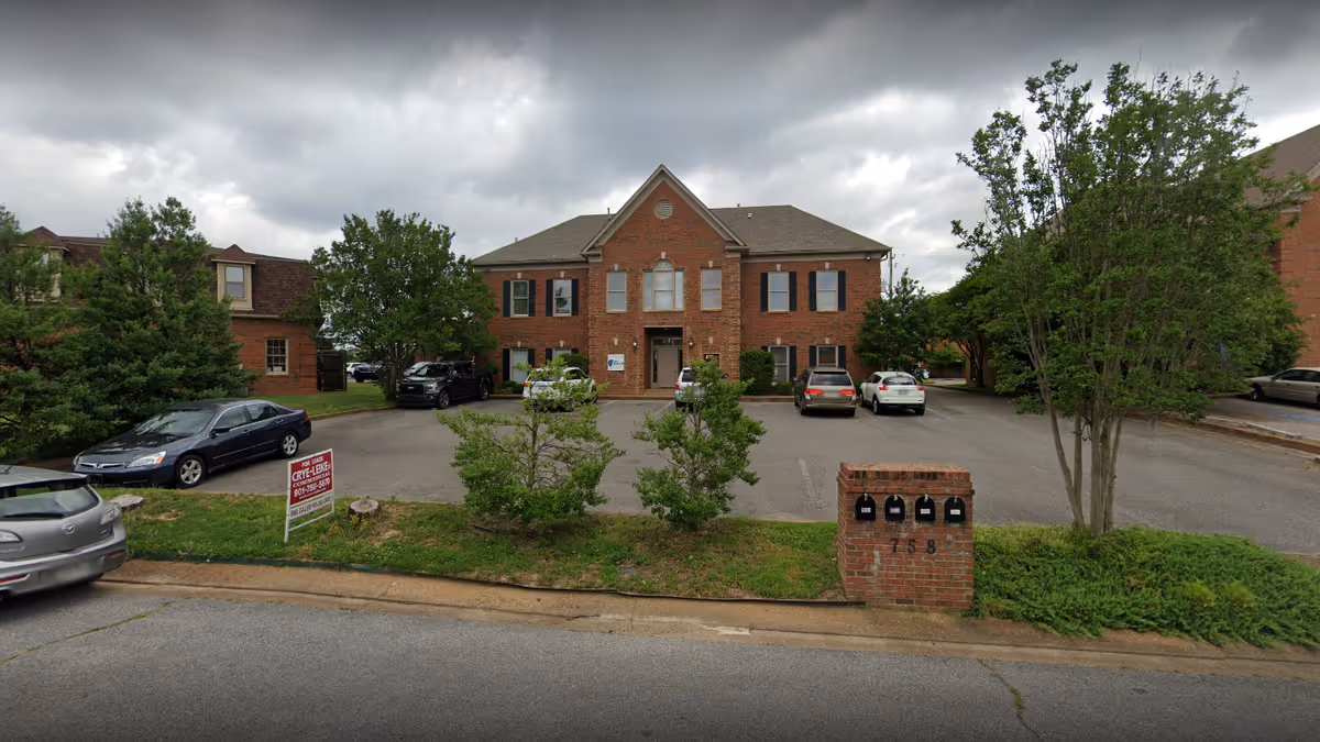 Brick senior living facility exterior with parking lot, trees, and a brick mailbox.