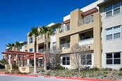 Front exterior of Healthcare Center of Bella Vista, a multi-story senior facility with palm trees.